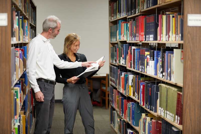 Reference Librarian Michael Current and UWL student using a book in the Reference Collection