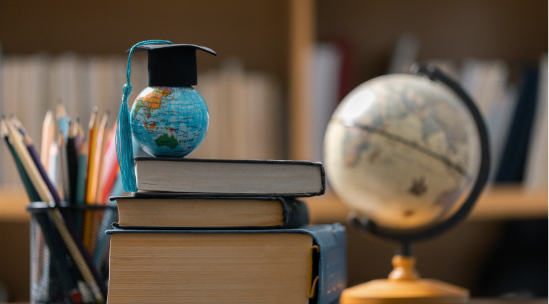 A small globe with a graduation cap on a stack of books. 