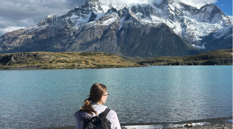 A person stands in front of a mountain and lake.
