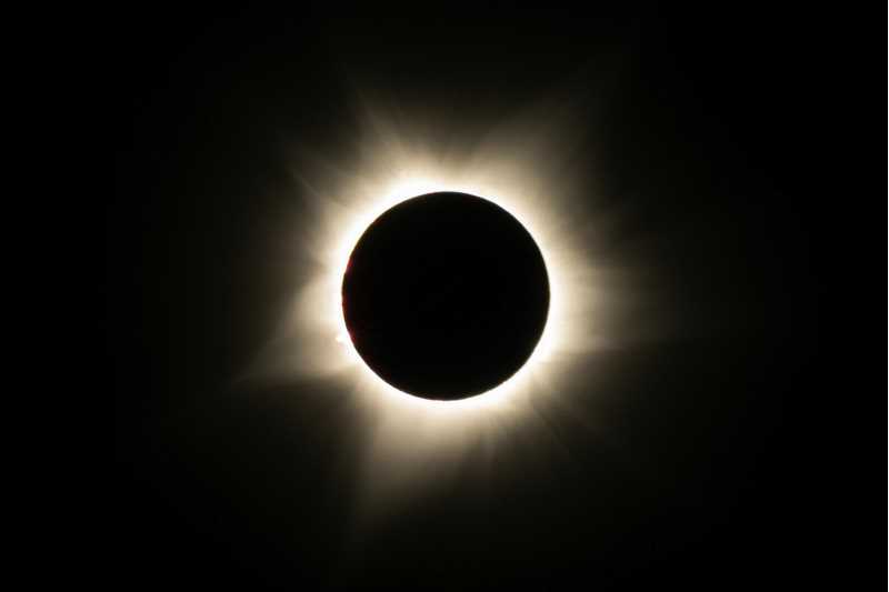 Total solar eclipse image where the sun is blocked out by the moon and only the solar corona is visible.