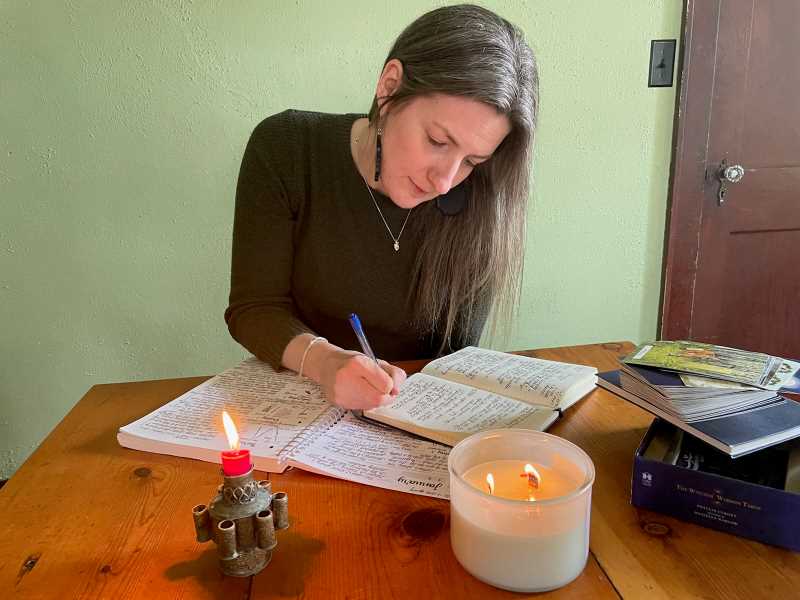 Dr. Kate Parker at home working in her journal with a tarot deck and candles.