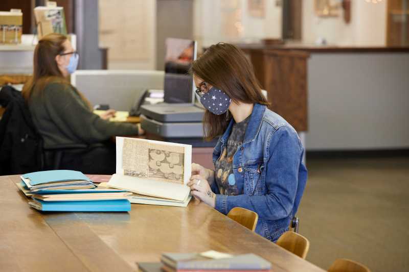 Student looking at archival material and wearing a mask in Special Collections