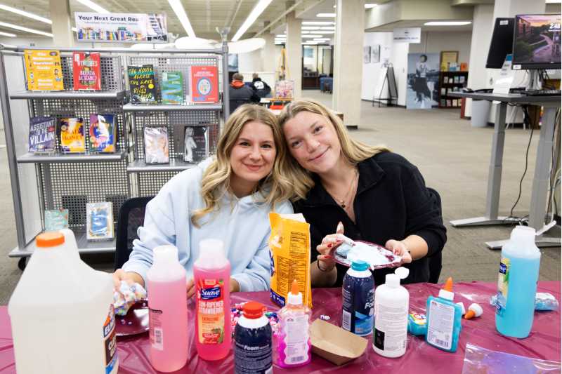 Alt text: Two students play with slime they made with UWL's Second Year Experience in Murphy Library.  
