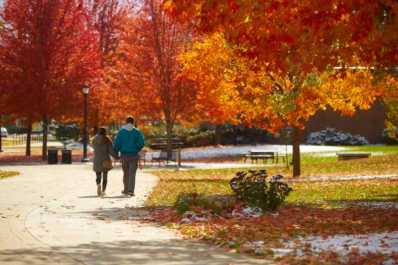 Two people walk together on campus in the fall.