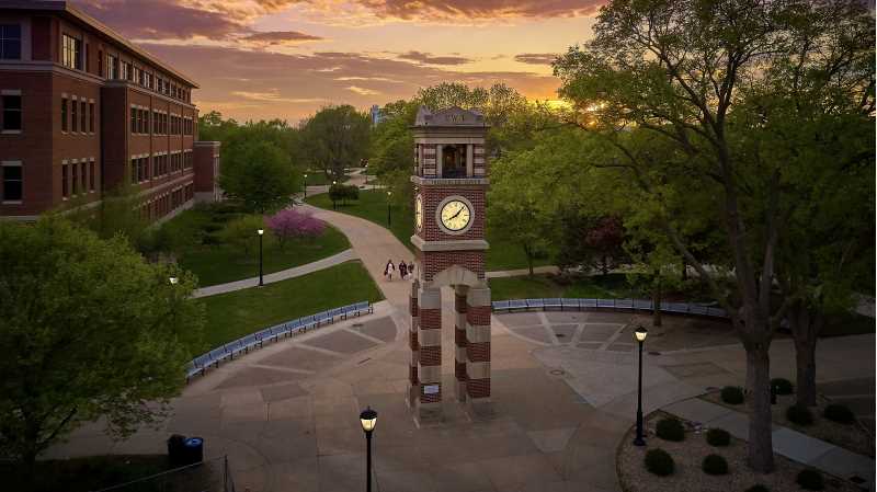 Students walk toward Hoeschler Tower in graduation regalia. 