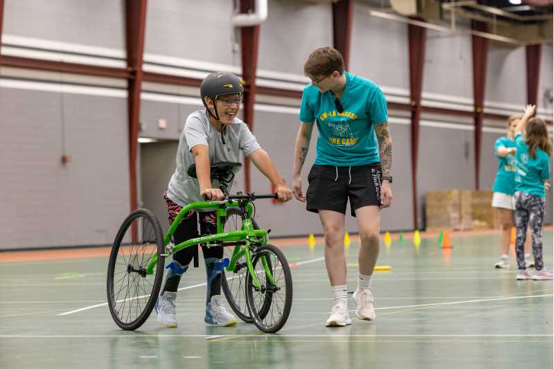 10-year-old Bentlee Cleveland rounds the track at Mitchell Hall on a three-wheel adaptive bike. UWL graduate student Mandi Lucas is showing Cleveland how to use it. 
