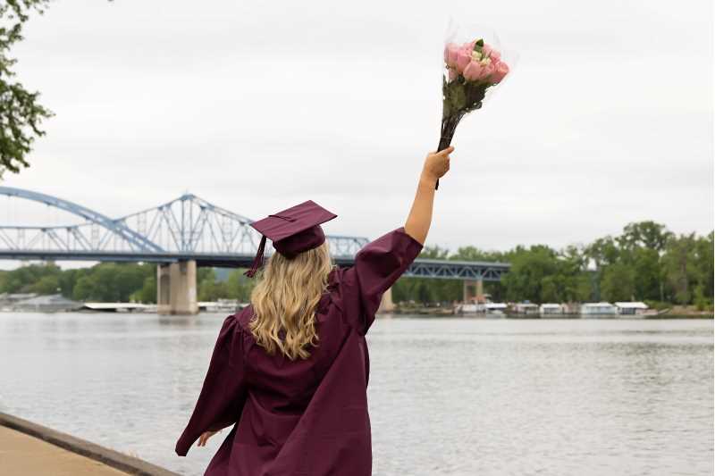 A spring 2025 UWL graduate holds a bouquet of flowers and looks out over the Mississippi River at Riverside Park following the commencement ceremony.