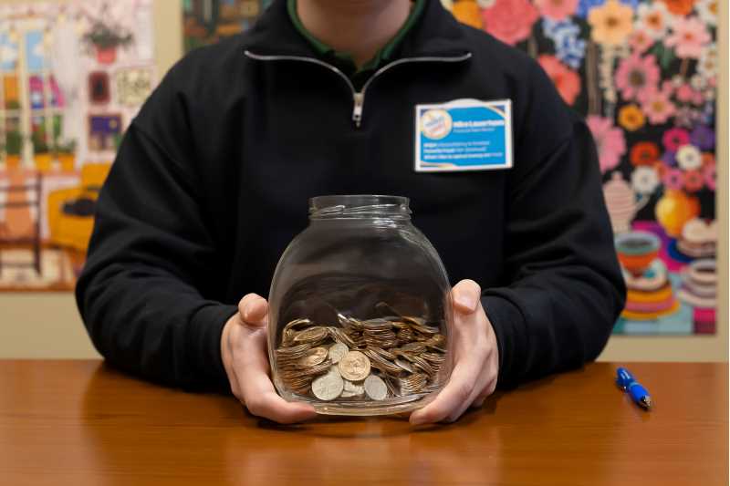 A student holds a jar of spare change, a simple reminder that small savings can add up over time.