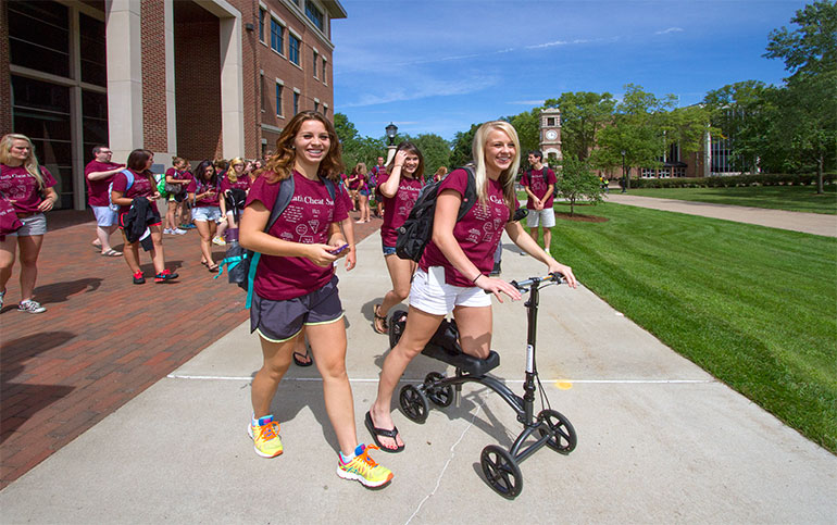 Students in maroon T-shirts. One on scooter.