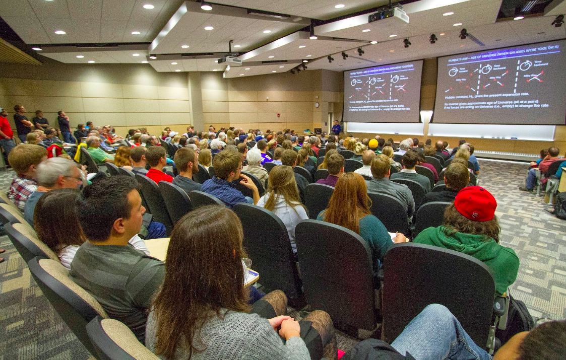 Image of Adam Reiss speaking to a large crowd in an auditorium at UW-L. 