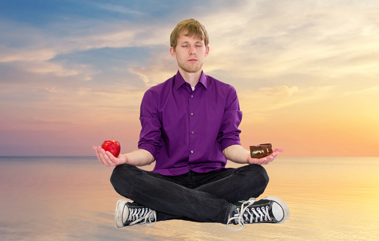 Photo of Eric Barreau sitting in a meditation pose and holding an apple and a piece of cake. 