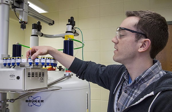 Image of Brian Peterson placing a tube in the Nuclear Magnetic Resonance (NMR) Spectrometer. 
