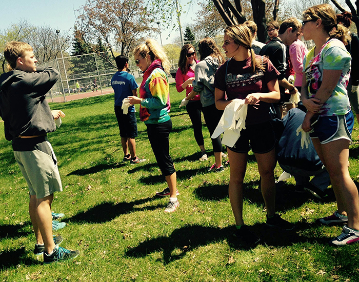 Image of students standing in grass putting their gloves on to pick up garbage. 