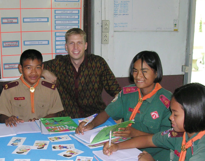 Hokenson poses with three students at a table with workbooks and flash cards.