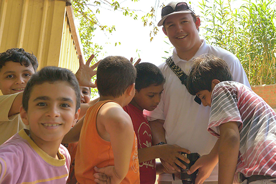 UW-L student Max Kaiser pictured holding a camera and surrounded by small children in Egypt. 