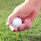 Hand pushing golf ball and tee into ground. 