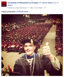 Joe Gow posing for a selfie with graduating class in the background at commencement. 