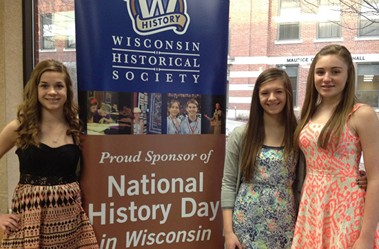 Three girls standing in front of the National History Day sign in Cartwright Center. 