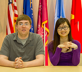 Image of Yen and Devan sitting infront of flags. 