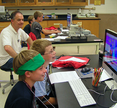 Boys in front of computer with teaching looking on. 