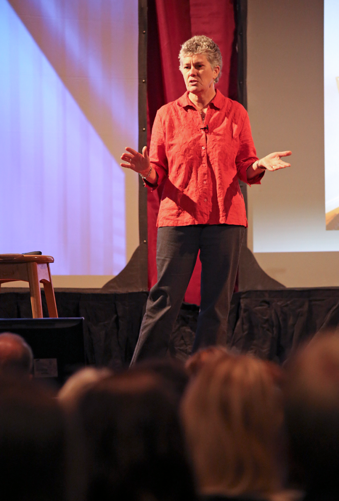 Elementary School Counselor Melani Fay speaking on Graff Main Hall auditorium stage. 