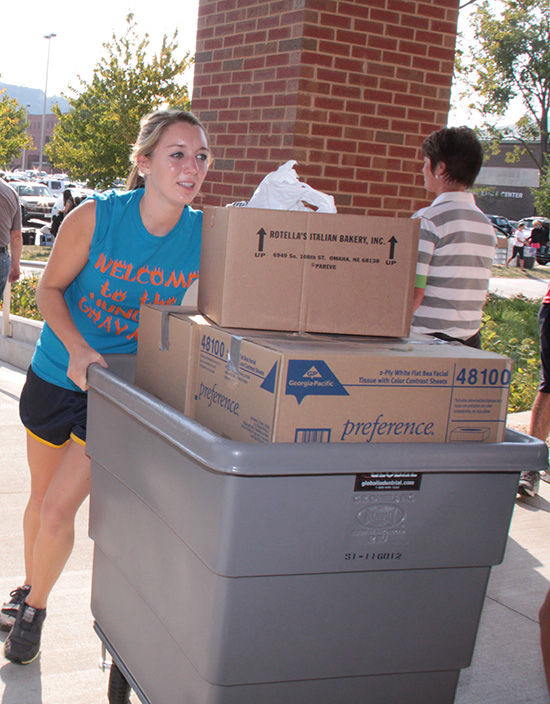 Student moving large crate with boxes in it near residence hall.