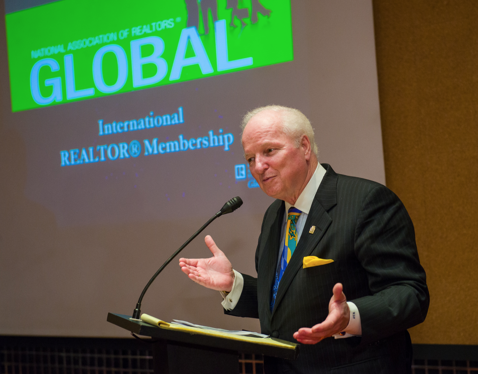 Norm Flynn speaking in front of a podium with lecture slides at a conference.