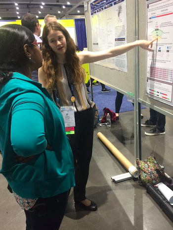 Gina Wade pointing at her poster while describing her research. 