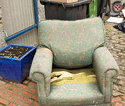Image of an old chair by a garbage can. 