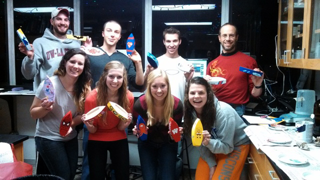 Image of Professor Scott Cooper and students holding up toy boats. 
