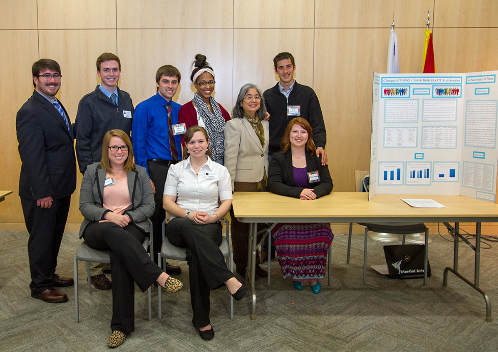 A group of students standing and sitting by posters. 