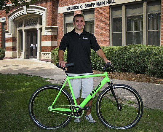 May graduate Wyatt Hrudka poses with bike outside Graff Main Hall.