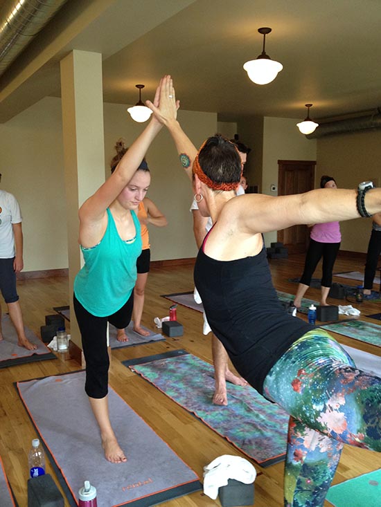 Students touching hands and leaning toward eachother in a yoga pose in the hot yoga studio, Root Down Yoga. 