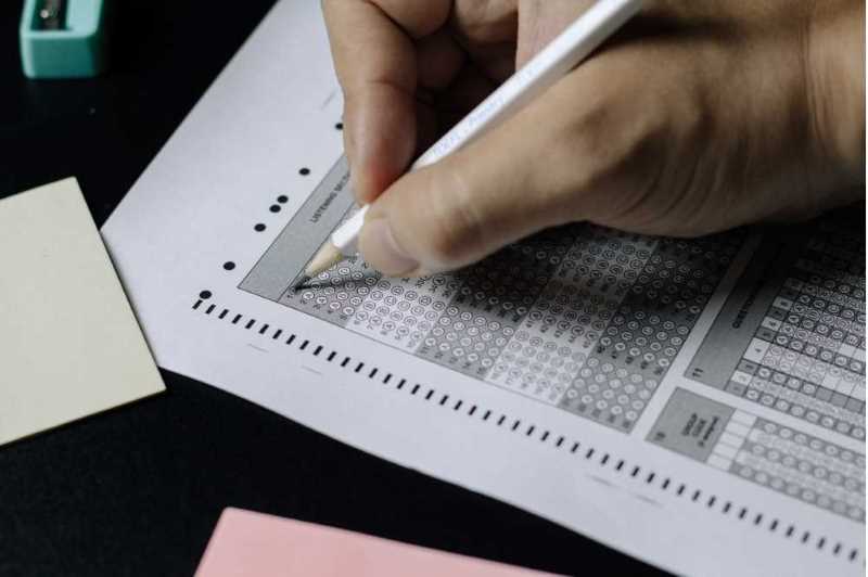 A hand holding a pencil filling in circles on a blank test sheet.