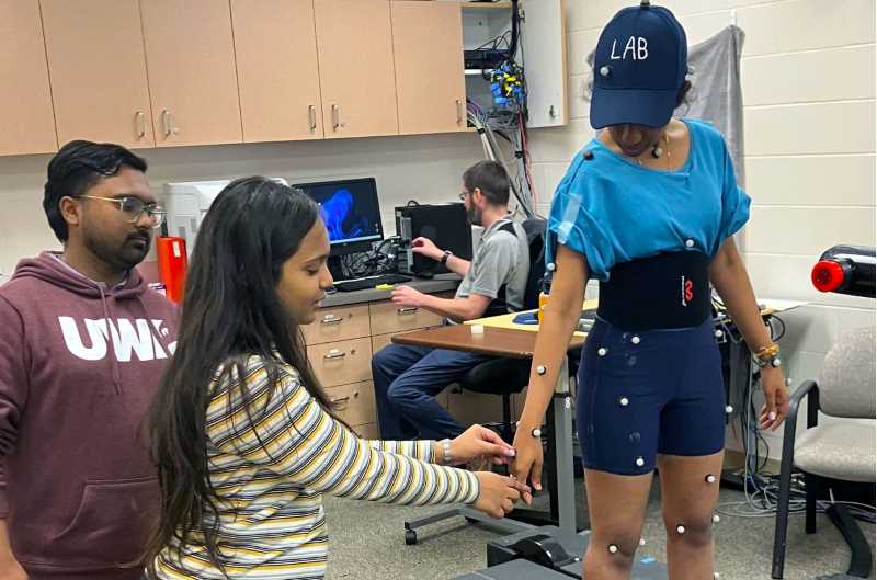 From left, students from the KLE Institute of Physiotherapy in Belagavi, India, Supriyo Sarkar and Shreyasi Ghatkar apply reflective markers on Anuradha Paramshetti, another student from KLE. Paramshetti stands on the force plate-embedded treadmill called Treadmetrix. 