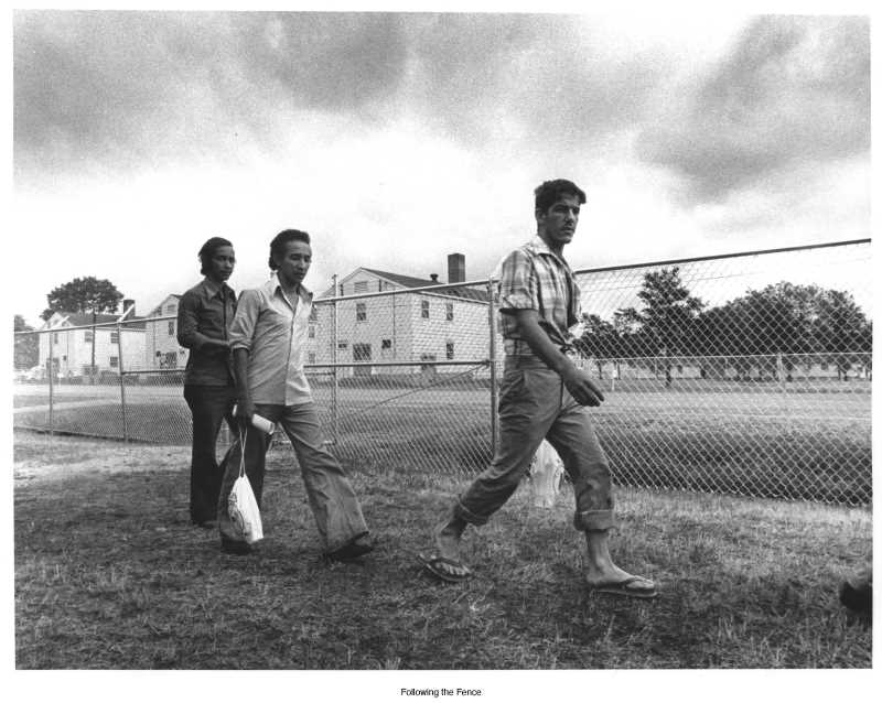 Refugees walk along a fence at Fort McCoy resettlement center. Nearly 15,000 Cuban refugees settled at Fort McCoy as part of the Mariel Exodus, a mass emigration of Cubans from Cuba's Mariel Harbor to the U.S. in 1980. Photo credit: Murphy Library Special Collections/ARC.