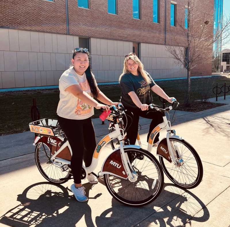 Two students on UWL logo bicycles on campus