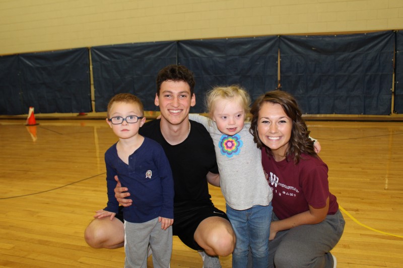Two Adapted Physical Education Teaching Minors smile with the children with disabilities they are holding.