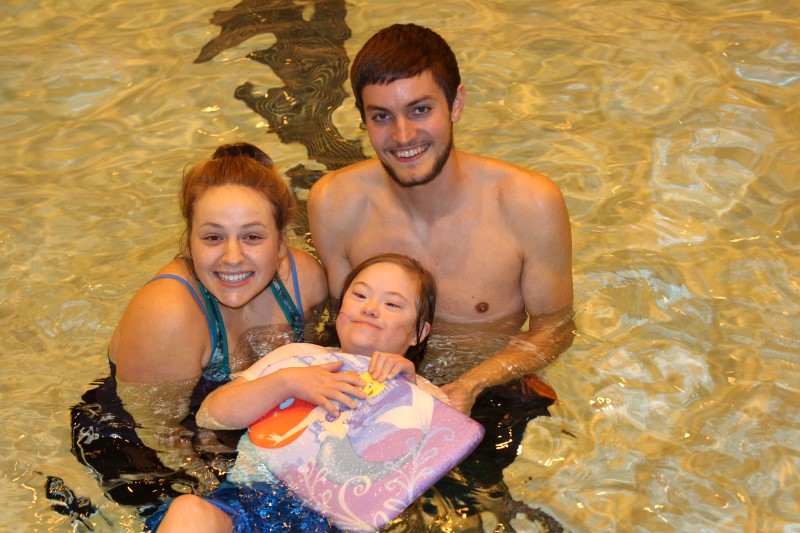 Two University Students help a girl with a disability float in the pool.