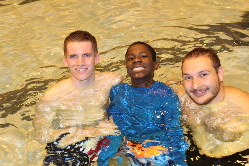 Two Adapted Physical Education Minors help a boy with a disability in the pool.