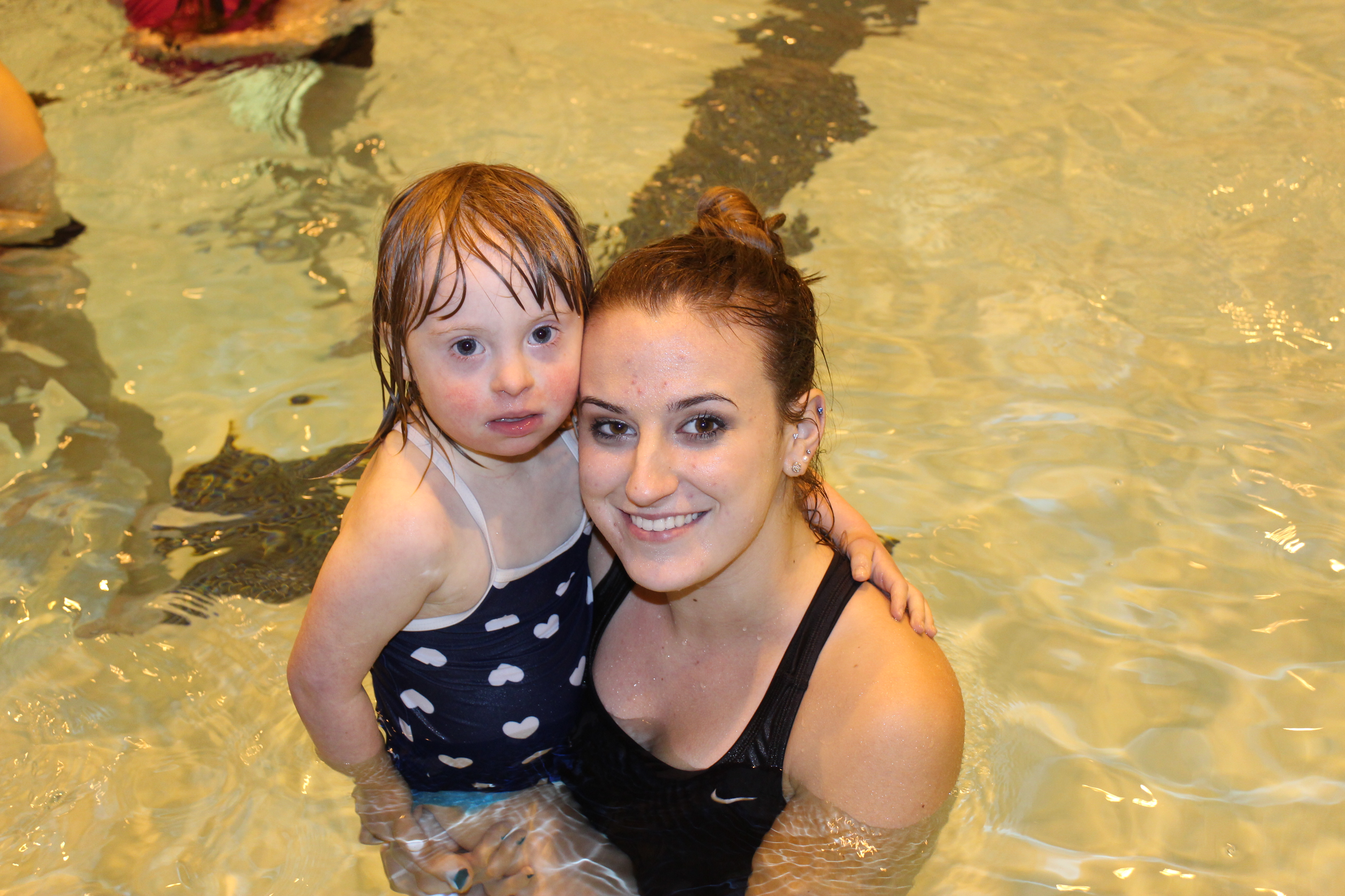 An Adapted Physical Education Teaching Minor holds a small girl with a disability in the pool.