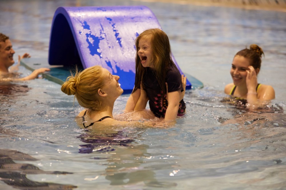 Child playing in the pool with a graduate student helping.