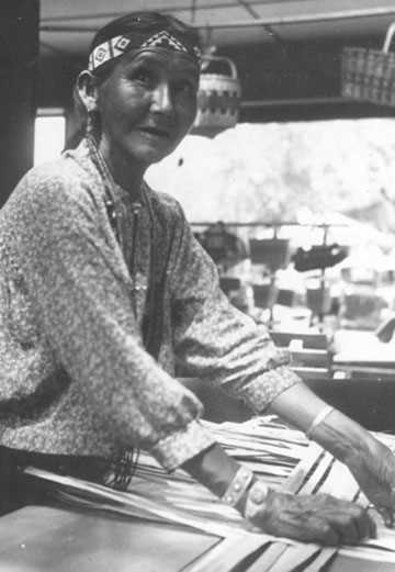 Susie Redhorn weaving the base of a basket wearing ornate jewelry.