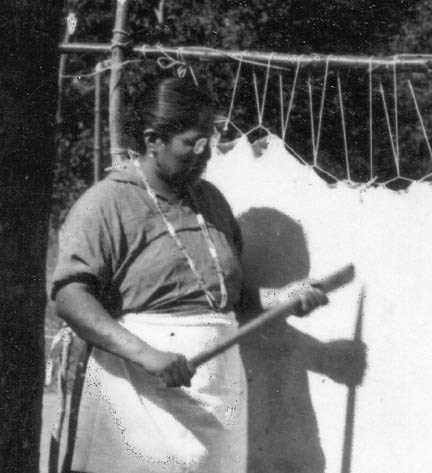 Lena Shegonee tanning a hide with wooden tool