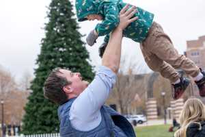 Parent plays with their child in front of the Campus Holiday Tree.