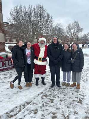 Chancellor Beeby outside in the snow at the clocktower with CBA students and Santa.