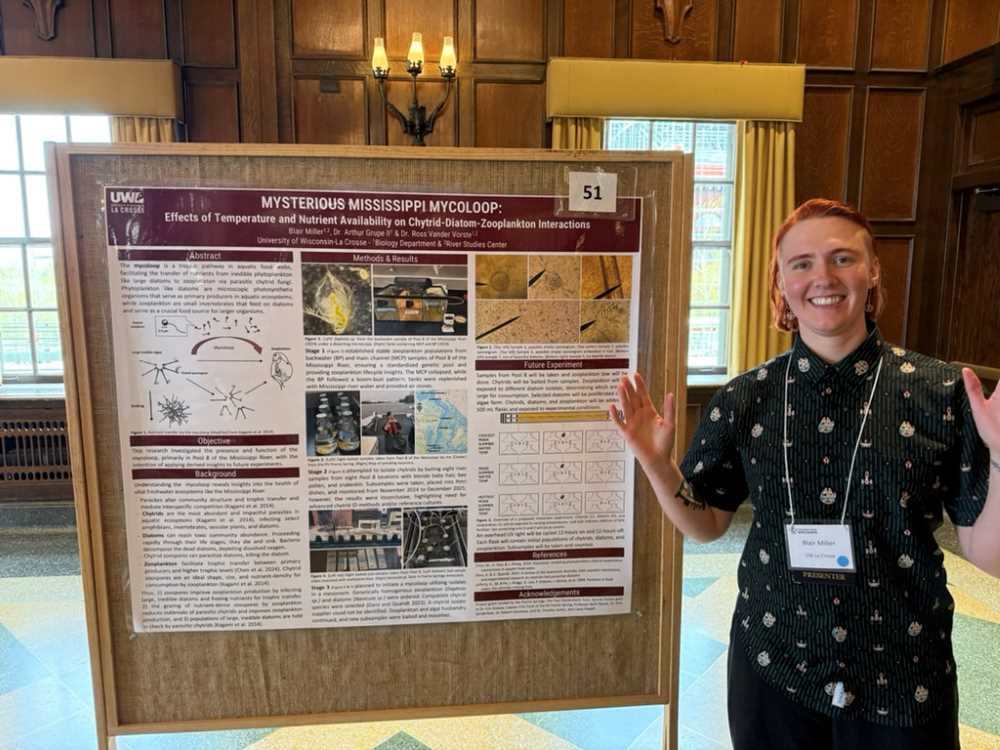 A student stands in front of their research poster