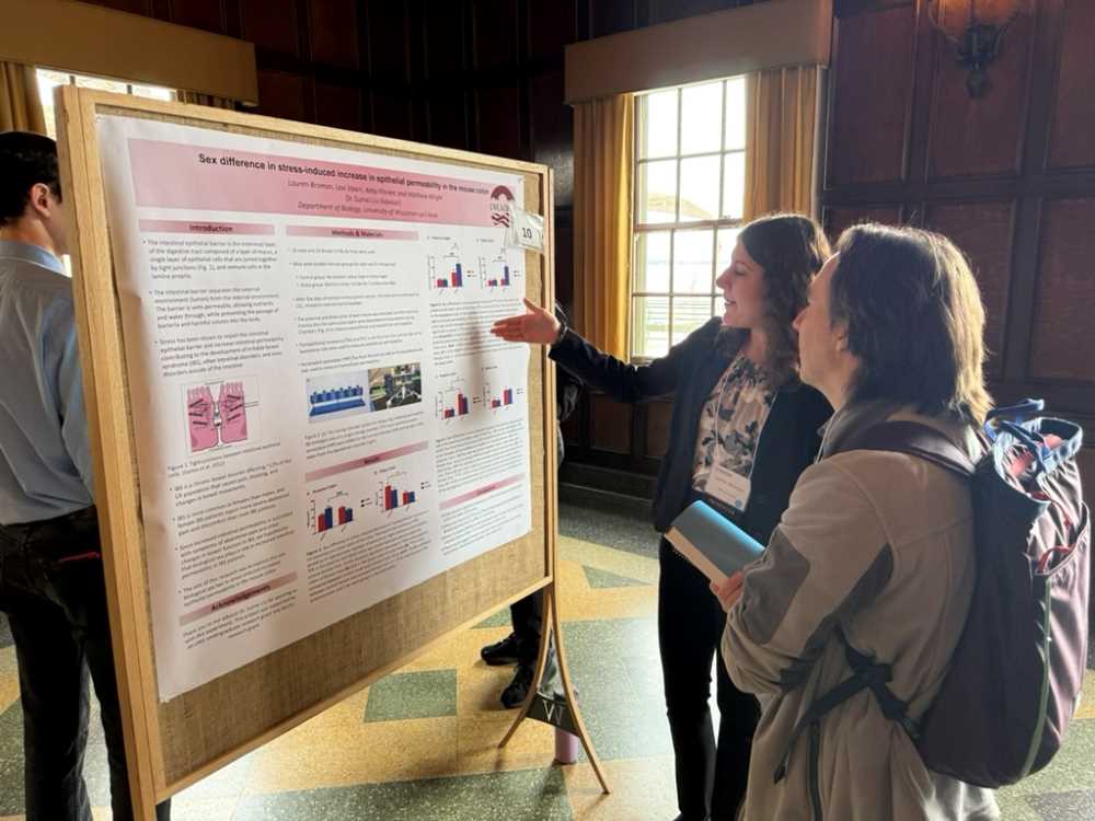 A student presents her research poster to an onlooker
