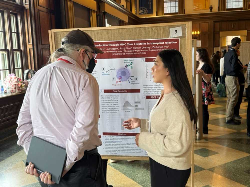 A student presents her research poster to an onlooker