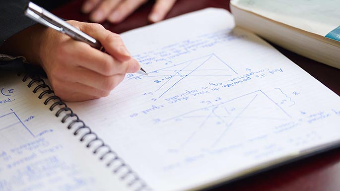 Image of a hand holding a pencil writing on a notebook